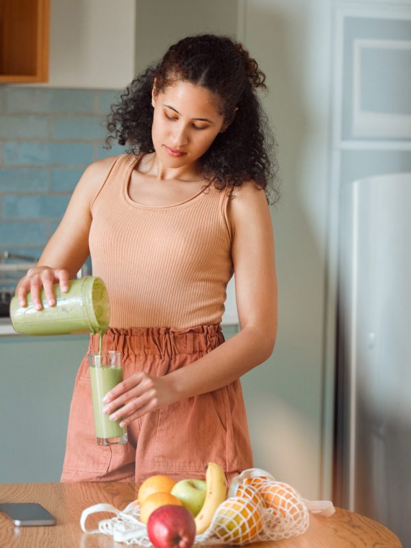 Healthy, nutrition and wellness lifestyle young woman making fresh, green detox fruit smoothie for .