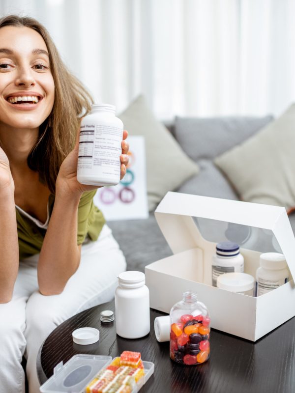 Portrait of a young smiling woman taking nutritional supplements at home. Concept of biohacking and preventive medicine