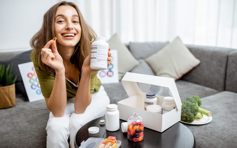 Portrait of a young smiling woman taking nutritional supplements at home. Concept of biohacking and preventive medicine