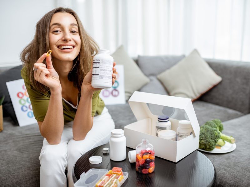 Portrait of a young smiling woman taking nutritional supplements at home. Concept of biohacking and preventive medicine